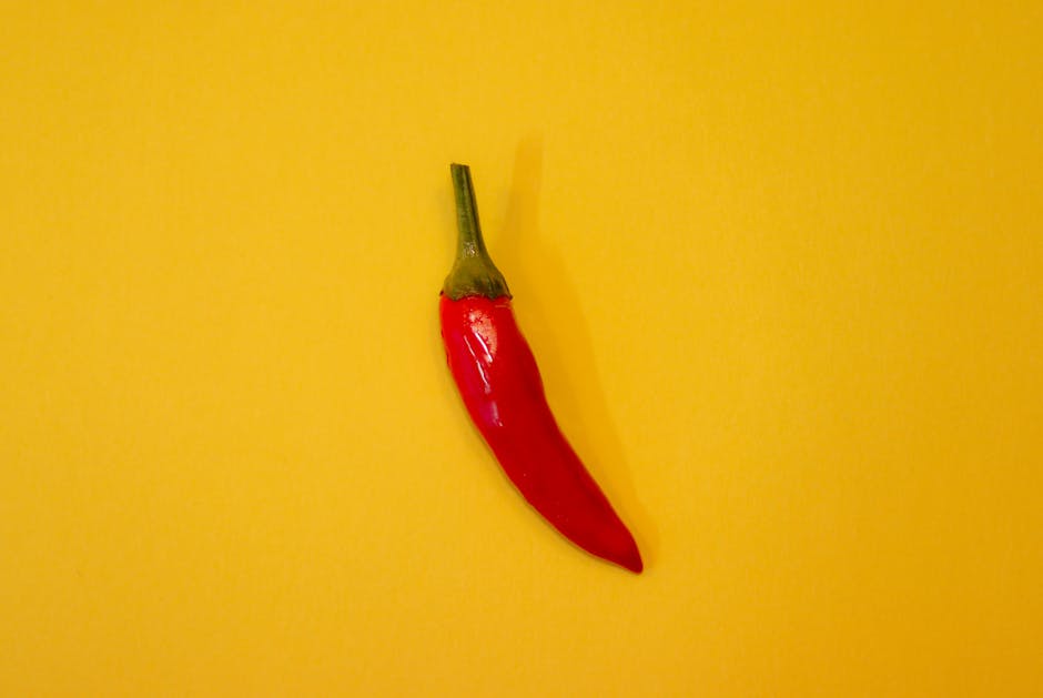 A single red chili pepper isolated on a vibrant yellow background, showcasing freshness and spice.